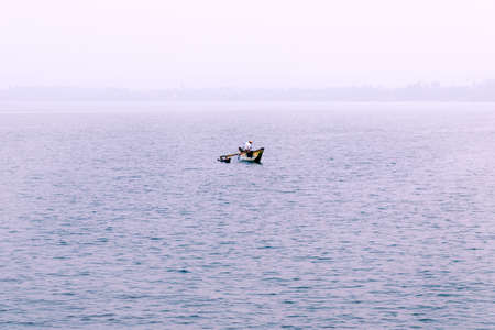 Foggy morning, a fisherman in a boat on the lake. Nature loneliness, solitude.の写真素材