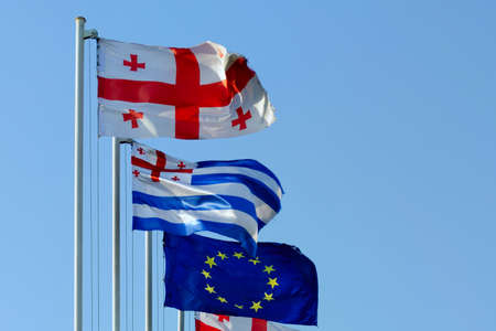 Flags of Georgia, Ajaria and the European Union fluttering in the wind against a blue sky.の写真素材