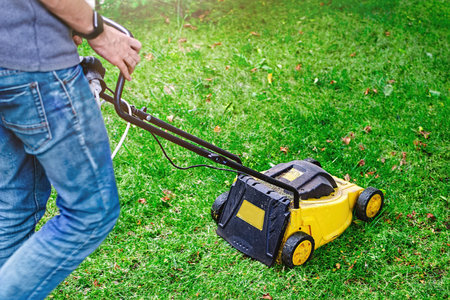 Man moving a lawn mower to cut the grass on the lawn.  Sunny autumn day.  Gardening work tool. ...