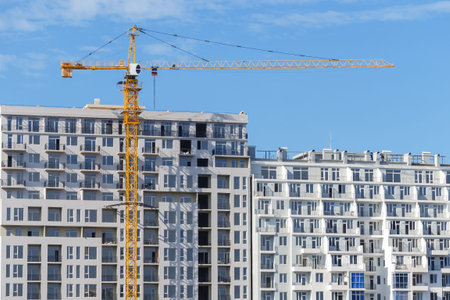 Tower crane construction on the background of a completed apartment building and blue sky.  A glut...