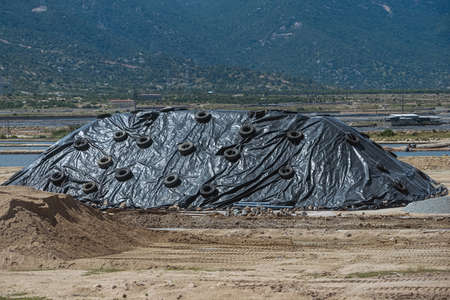 Storage warehouse of mineral construction materials in outdoors.  Pile of rubble is covered with a protective film from the weather. Industrial concept and construction background.の写真素材