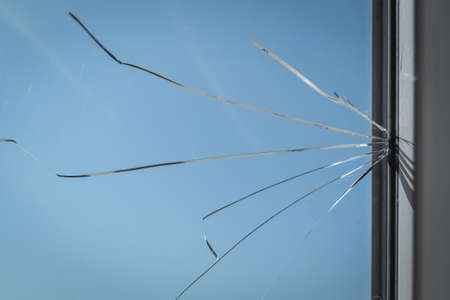 Cracked glass in the window frame of the house. Damaged window as a consequence of vandalism or natural disasterの写真素材