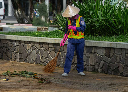 Municipal worker sweep the street with broomstick. City street janitor makes sanitation.  Nha Trang, Vietnam: 2020-10-18.のeditorial素材