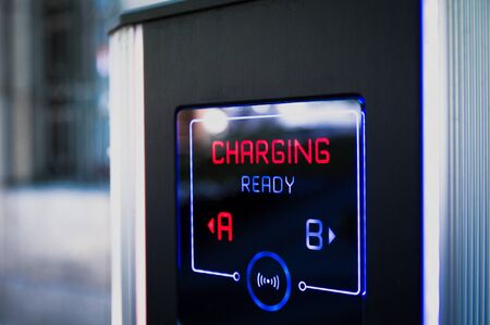 Electric car charging station in city parking with active Charging sign in red colorの写真素材