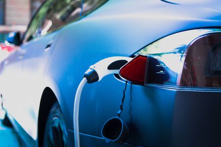 Charging modern electric car with cable plug inserted ir parking lotの写真素材