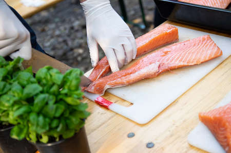 Man hands cutting pink raw salmon with knife on boardの写真素材