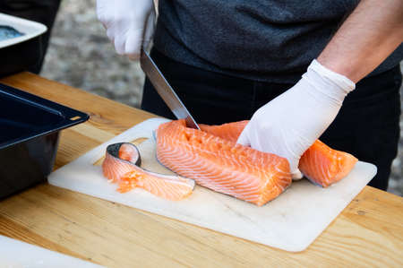 Man hands cutting pink raw salmon with knife on boardの写真素材