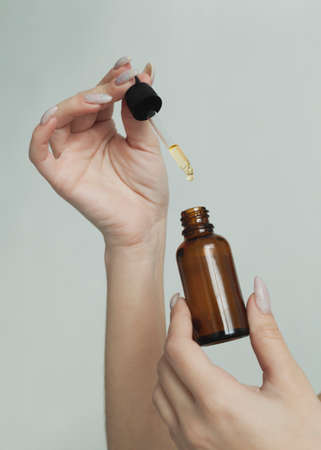 a bottle of facial serum in the hands of a girl on a light backgroundの写真素材
