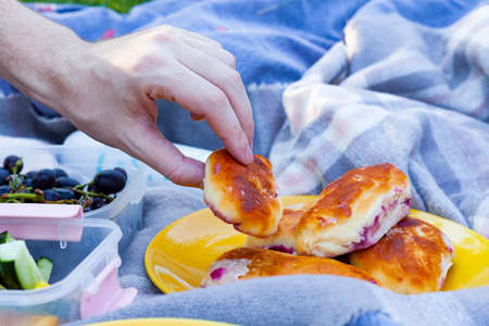 a man on a picnic takes sweet pastries from a plate. Detailed food photoの写真素材