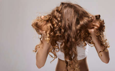 a woman with long well-groomed curly hair stands on a gray background and demonstrates themの写真素材