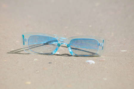blue sunglasses from the sun lie on the sand near the sea in sunny weatherの写真素材