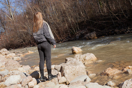 a woman stands near the river in warm clothes, walking in sunny weather. Topics of an active lifestyleの写真素材