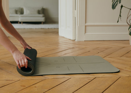 a woman rolls out a yoga mat at homeの写真素材