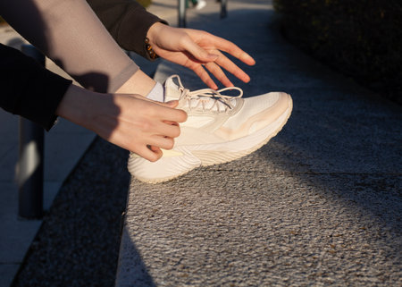 a woman ties her shoelaces on sneakers while jogging in the parkの写真素材