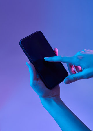 a woman's hand holds a smartphone touching the screen with her fingers on a colored backgroundの写真素材