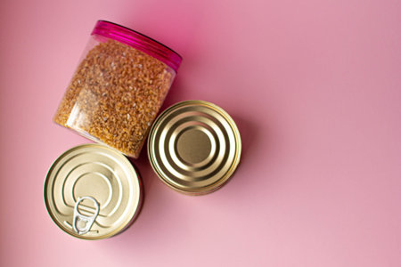 Dry porridge and canned food on a pink background.の写真素材