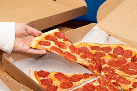 The hand takes a piece of pizza from the box. Sliced pizza in a box. food delivery.