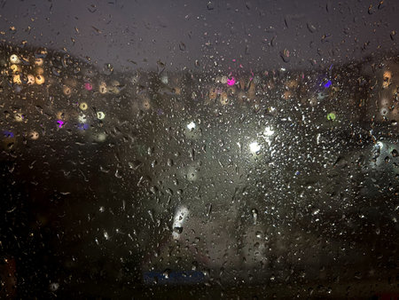 The window is wet from rain. Night city behind wet glass. Urban Theme Background.
