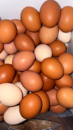 Vertical photo.A close-up shot of many fresh farm-fresh chicken eggs, haphazardly piled in a heap.