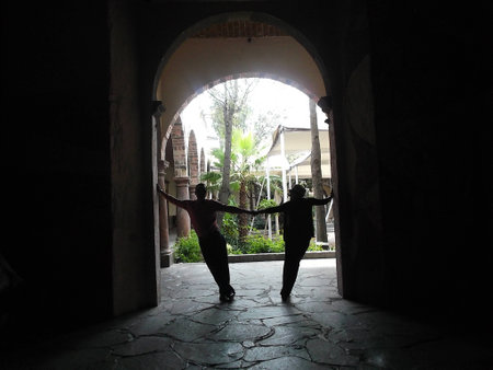Silhouette of a couple, arms reaching out, holding each others hand under an archの写真素材