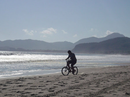 Silhouette of a person riding a bike on the beachの写真素材