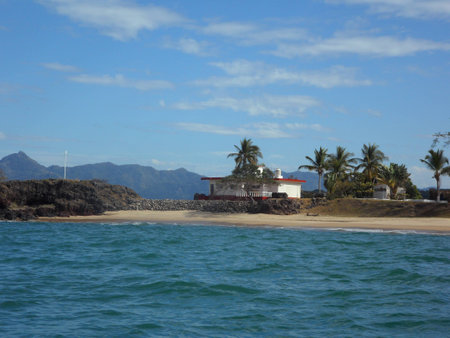 Frontal view, from the sea, of a house on the beach surrounded by sand and palm treesの写真素材