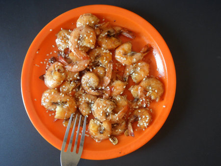 Cooked, unpeeled, shrimps with oil and sesame seeds, served on an orange dish over a blue backgroundの写真素材
