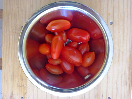 Grape tomatoes in a metal bowl on a wooden table. Top view.の写真素材