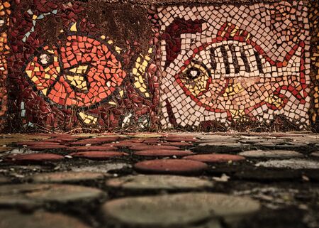 An old mosaic in the form of a fish on the wall of a decoratively dried pool is overgrown with grass. Background with copy spaceの写真素材