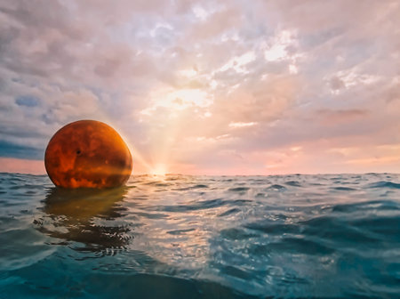 An orange buoy floats on the sea waves in the rays of the setting sun against a sunset cloudy sky....
