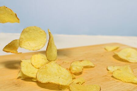 Natural potato chips fall on a wooden cutting board lying on the table. Close to copy space.の写真素材