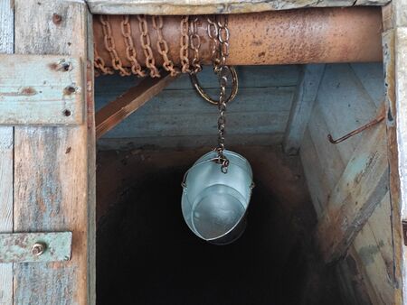 Empty metal bucket hanging on a chain, over the well.の写真素材