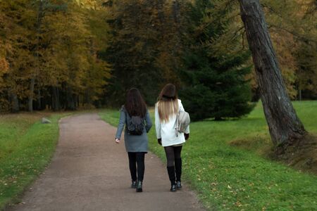 Two girls with backpacks walk along a dirt path along an alley in a summer parkの写真素材