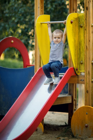 Little boy is ready to skate from the playground slides. Cheerful little boy having fun while sliding outdoors.の写真素材