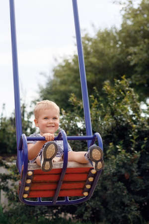Happy, smiling child is swinging on a swings in a park at summerの写真素材
