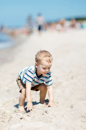 A little boy in a striped shirt, crawling on the beach sand, he learns to walk.の写真素材