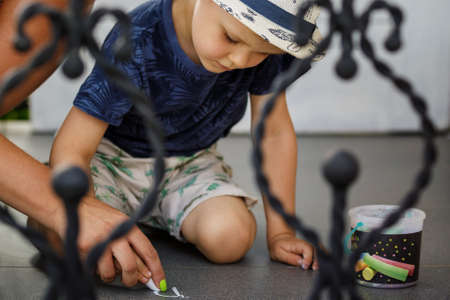 Little boy and his mother drawing with colorful chalk crayons on concrete sidewalk top view. The mother helps to concentrate with the help of her hand, she teaches her childの写真素材