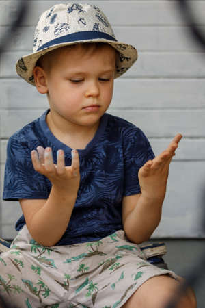 A little boy in a white hat looks at his hands, which he smeared when he drew with colored crayonsの写真素材