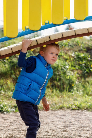 A little cute boy plays under a beautiful, curved bridge on a colorful playground. An agile child...