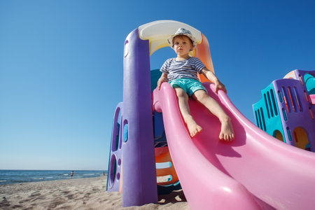 Colorful plastic slide on the beach background, cute little boy getting ready to slide downの写真素材