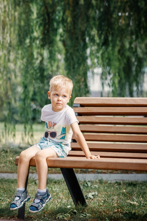 Child portrait sitting on a bench in park, white haired boy 3 years old. Front view, vertical photo.の写真素材