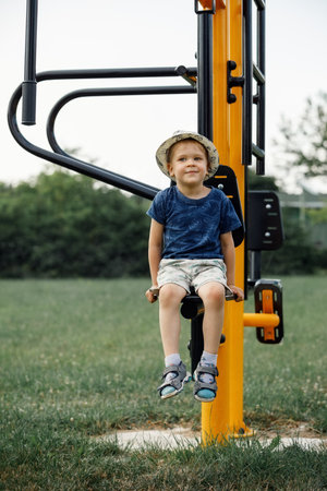 Boy athlete on outdoor sports ground. Child sitting on yellow outdoor exercise machine for teenagers.の写真素材