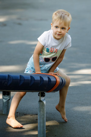 Portrait of a little boy in an outdoor sports gym, a child performs gymnastic exercises barefoot on modern equipment.の写真素材