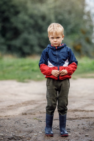 Portrait of a sad lonely boy in bad weather in autumn. The end of summer fun. Dirt and humidity outdoors there is no activity for children.の写真素材