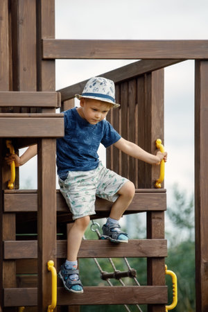 The boy is playing on an outdoor playground, he climbs a wooden ladder dangerously. An active child needs parental care for safety.の写真素材