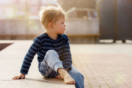 Little boy sitting by the fountain on a Sunny day, the child looks into the distance, there is free space for text in the picture.の写真素材