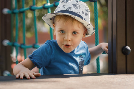 Cute little boy playing on the playground in the summer. A portrait of a child in a hat looks straight into the camera with a surprised facial expression.の写真素材