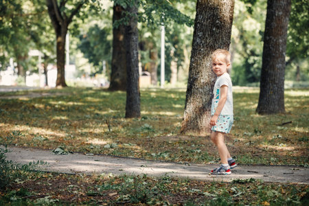 A little cute boy walks in a city park, a beautiful summer sunny day, big oak trees around.の写真素材