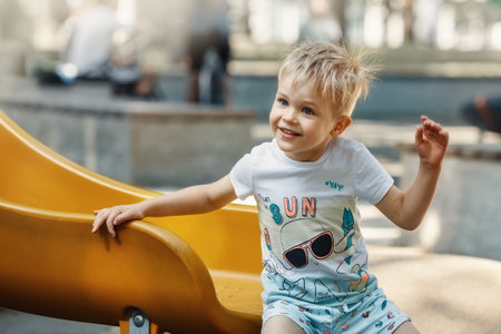 A cheerful, smiling, likeable little boy on the playground on a yellow slider. The child's hair is electrified and bristling.の写真素材