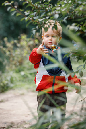 The little boy plays with soap bubbles in nature, the child tries to catch a colorful soap bubble by hand.の写真素材
